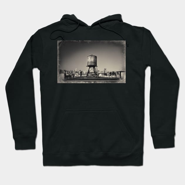 Sepia-toned image of a rusty water tower on a rooftop of Queens, in New York City, with the Queensboro Bridge and the Manhattan skyline in the background. Hoodie by Reinvention